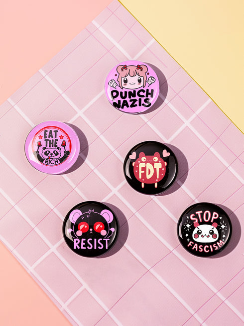 A set of five glossy round pinback buttons with pastel goth and kawaii punk designs, featuring slogans like "Eat The Rich" and "Stop Fascism" in bold pink and black. Each pin has a cute character with a rebellious message.