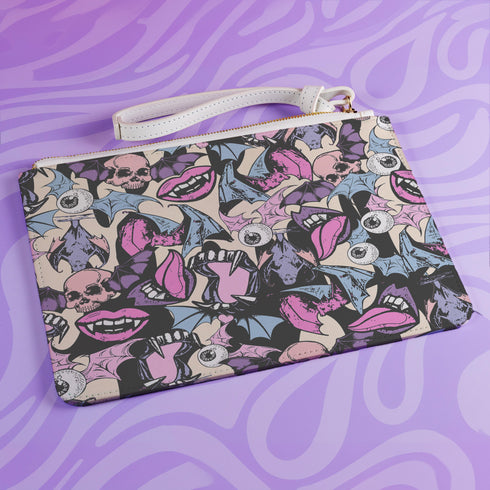 Rectangular wristlet clutch featuring a dark background with colorful bats, skulls, eyeballs, and vampire mouths. White strap and gold zipper visible.