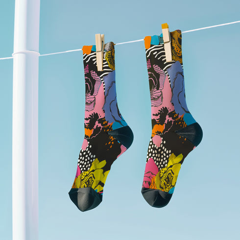 Colorful crew-length socks with a vibrant floral pop-art collage design, featuring abstract roses in yellow, lavender, pink, and orange tones, polka dots, and zebra stripes on a black background.