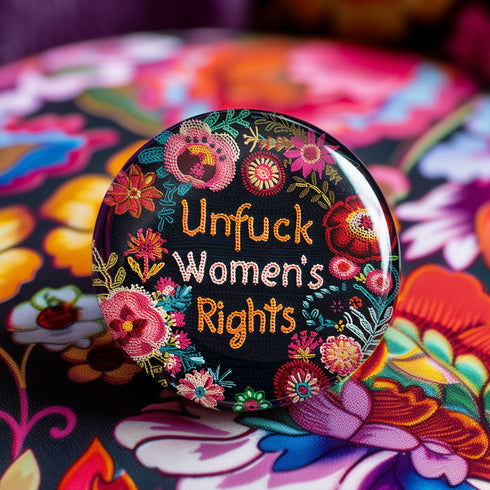 Round pinback button with black background featuring vibrant floral embroidery design surrounding bold orange and white text reading "Unfuck Women's Rights" - feminist protest accessory with glossy finish, safety pin backing, available in 2" and 3" sizes for jackets, bags, and activist wear.
