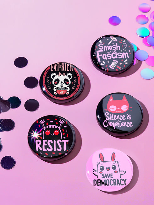 A set of five glossy round pinback buttons with pastel goth and kawaii punk designs, featuring slogans like "Eat The Rich" and "Smash Fascism" in bold pink and black. Each pin has a cute character delivering a powerful message.