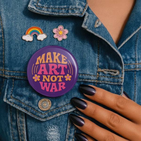 A round, glossy purple pinback button with the words "MAKE ART NOT WAR" in a groovy, retro 70s-style font. The word "MAKE" is in orange, "ART" is in a vibrant pink, and "NOT WAR" is in orange. The text is surrounded by small, stylized flower and star details. This psychedelic protest pin is a piece of activist merch with a strong metal back and safety pin clasp, perfect as an anti-war or social justice accessory for a jean jacket or backpack. The pin has a handmade, indie aesthetic.