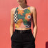 Cropped racerback tank top featuring bold retro floral print with orange and yellow mod flowers, green leaves, black and white checkerboard pattern, and abstract wavy designs. Fitted athletic style crop top in vibrant 70s inspired botanical print with performance fabric construction. Women's festival rave wear cropped camisole with psychedelic flower power design perfect for summer concerts, Y2K fashion looks, and alternative streetwear styling.