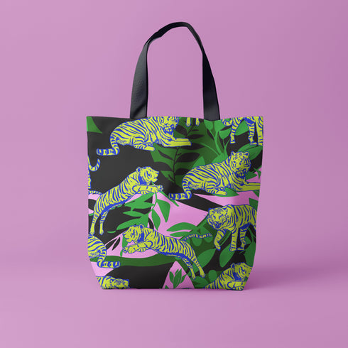 Tote bag with black handles featuring vibrant yellow and blue tigers on a background of pink and black with green foliage