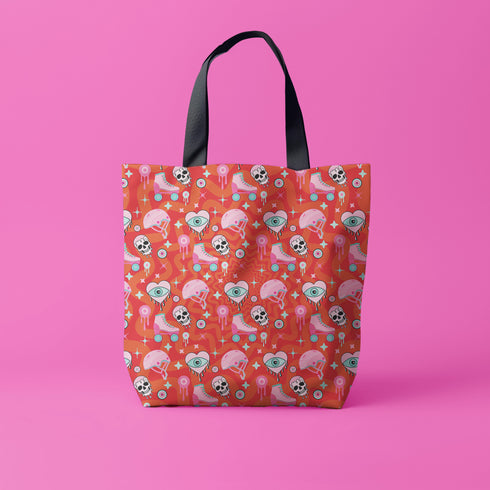 Tote bag with black handles featuring a vibrant red background covered in pastel pink and blue illustrations of skulls, roller skates, eyes, and geometric shapes. Displayed on an orange surface with dramatic shadows.