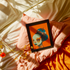Avant-garde digital portrait of an African woman with striking features against a vivid orange background. An elaborate headdress of dark, floral elements creates a stunning contrast, embodying surrealist themes and African cultural motifs.