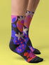 Black crew socks featuring an oversized, abstract strawberry pattern in bright pink, blue, and orange.