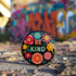 Bold "BE KIND" pinback button featuring vibrant psychedelic flowers in hot pink, teal, yellow, and orange on black background. Retro 70s-inspired typography in coral and mint green surrounded by colorful blooms. Statement activist accessory perfect for punk fashion, protest wear, and battle vests. Glossy UV-resistant finish with safety pin backing available in 2" and 3" sizes.