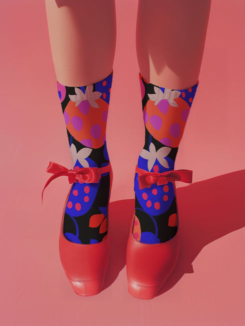 Black crew socks featuring an oversized, abstract strawberry pattern in bright pink, blue, and orange.