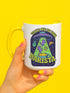 White ceramic coffee mug with a bright yellow handle and interior, featuring a printed alien abduction design with two purple cats, peace signs, and the phrase “Take Me to Your Barista” in green and purple text.