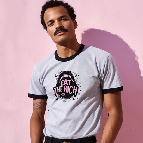 Off-white ringer t-shirt with black contrast trim on the collar and sleeve cuffs. The front features a bold, high-contrast graphic of an open mouth with the phrase "EAT THE RICH" in capital letters, styled in a hand-drawn font. The design is rendered in black and vibrant pink, with expressive line details surrounding the mouth, adding a dynamic, rebellious feel. The t-shirt has a vintage-inspired fit, made from soft cotton fabric with a slightly relaxed silhouette. The black trim enhances the retro aestheti