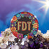 Circular black pinback button with bright 'FDT' lettering in orange/teal surrounded by colorful embroidery-style flowers in red, purple, blue, and yellow. Metal safety pin backing visible on reverse side. Political protest pin with vibrant Mexican folk art-inspired floral design.