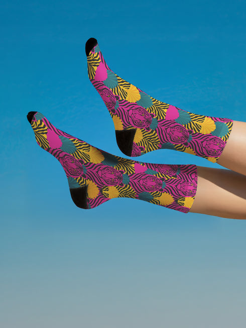 Colorful pink tiger print crew socks with black heel and toe, featuring yellow zebra stripes and teal and coral fan-shaped accents. Made of stretchy knit with a bold maximalist aesthetic. One size fits most, mid-calf length, vibrant all-over print