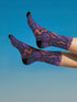 Mid-calf socks with a dark violet-black base featuring a gothic dagger and rose design in gradient shades of red, purple, and pink, with black heels and toes and an illustrated snake detail.