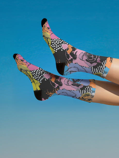 Colorful crew-length socks with a vibrant floral pop-art collage design, featuring abstract roses in yellow, lavender, pink, and orange tones, polka dots, and zebra stripes on a black background.