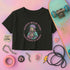 Black cropped t-shirt featuring a colorful, stylized saint figure with pink hair, wearing a helmet and pads. Surrounded by radiant lines and the phrase “Saints Wear Pads Catching Elbows” in bold pastel text. The design has a vintage punk-meets-holy aesthetic with star accents and a retro vibe. Ideal for roller skate girls, derby athletes, and goth skater fans. Available in sizes XS–2XL with raw hem details.