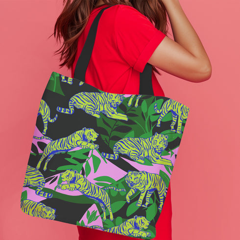 Tote bag with black handles featuring vibrant yellow and blue tigers on a background of pink and black with green foliage