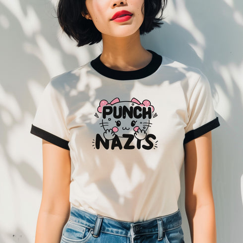 Off-white ringer t-shirt with black contrast trim on the collar and sleeve cuffs. The front features a bold, kawaii-inspired graphic of a cute cat with pink bows, blushing cheeks, and an assertive expression. Above the cat, the phrase "PUNCH" is written in bold, black capital letters, while below, "NAZIS" is displayed in a matching bold font. The cat’s paws are raised, playfully flipping off the viewer, adding a rebellious edge to the design. The t-shirt has a vintage-inspired fit, made from soft cotton fab