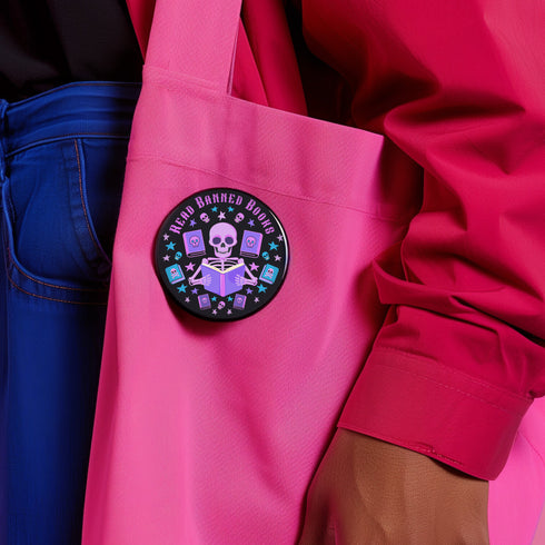 Literary rebel's badge of honor. Black circular button featuring a neon purple skeleton surrounded by floating books and stars. The text 'READ BANNED BOOKS' arcs across the top in bold purple lettering. Perfect for book-loving misfits who devour forbidden knowledge.