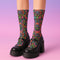 Colorful mid-calf socks with a black background featuring a whimsical folk-art bat pattern in rainbow tones of pink, orange, teal, and green, paired with matching heels and toes.