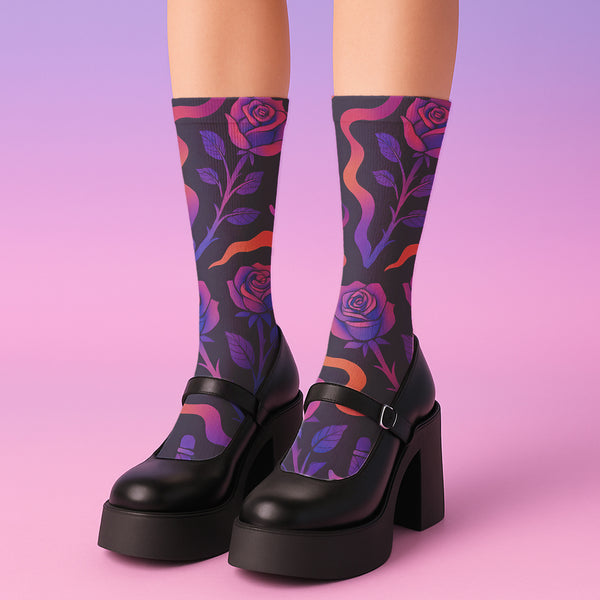 Mid-calf socks with a dark violet-black base featuring a gothic dagger and rose design in gradient shades of red, purple, and pink, with black heels and toes and an illustrated snake detail.