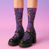 Mid-calf socks with a dark violet-black base featuring a gothic dagger and rose design in gradient shades of red, purple, and pink, with black heels and toes and an illustrated snake detail.