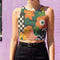 Cropped racerback tank top featuring bold retro floral print with orange and yellow mod flowers, green leaves, black and white checkerboard pattern, and abstract wavy designs. Fitted athletic style crop top in vibrant 70s inspired botanical print with performance fabric construction. Women's festival rave wear cropped camisole with psychedelic flower power design perfect for summer concerts, Y2K fashion looks, and alternative streetwear styling.