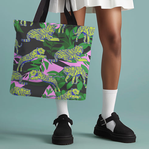 Tote bag with black handles featuring vibrant yellow and blue tigers on a background of pink and black with green foliage