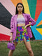 Vibrant mini skirt featuring an eye-popping psychedelic print of melting smiley faces and skulls in neon pink, bright yellow, electric blue, and lime green. The skirt has a distinctive side slit and sits above knee-length with a figure-hugging silhouette. Shown styled with various tops including a black crochet halter, black bustier, and purple blazer against colorful graffiti backdrops. The bold pattern makes this an unmissable statement piece with serious punk-meets-pop-art attitude.
