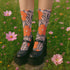 Colorful mid-calf crew socks featuring a bold orange hibiscus floral pattern layered over wavy zebra stripes in taupe and gray, with black heels and toes.