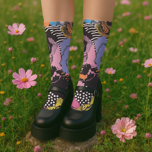 Colorful crew-length socks with a vibrant floral pop-art collage design, featuring abstract roses in yellow, lavender, pink, and orange tones, polka dots, and zebra stripes on a black background.