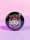 A round, black pinback button with a high-gloss finish features the text "THE FUTURE IS FEMME & FERAL" in a retro font of lime green and pastel pink. In the center, a screaming possum with wild eyes and a pink-lined mouth is illustrated in a pastel goth style with purple, yellow, and pink fur. The possum wears a pink flower crown. The illustration is framed by a circle of small skulls and pink Venus (female) symbols on a purple background. This is a piece of feminist possumcore flair.
