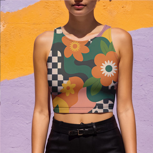Cropped racerback tank top featuring bold retro floral print with orange and yellow mod flowers, green leaves, black and white checkerboard pattern, and abstract wavy designs. Fitted athletic style crop top in vibrant 70s inspired botanical print with performance fabric construction. Women's festival rave wear cropped camisole with psychedelic flower power design perfect for summer concerts, Y2K fashion looks, and alternative streetwear styling.