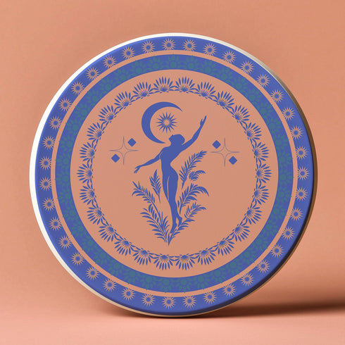 Round ceramic coaster featuring a silhouetted dancing figure reaching toward a crescent moon, surrounded by concentric rings of stars and floral patterns in blue on peach background