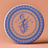 Round ceramic coaster featuring a silhouetted dancing figure reaching toward a crescent moon, surrounded by concentric rings of stars and floral patterns in blue on peach background