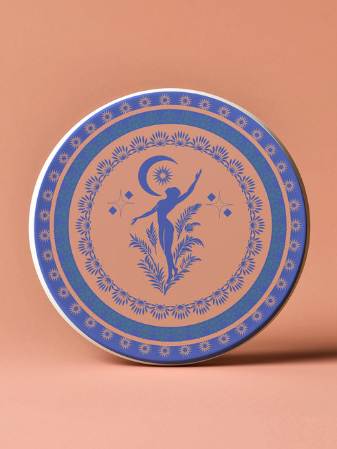 Round ceramic coaster featuring a silhouetted dancing figure reaching toward a crescent moon, surrounded by concentric rings of stars and floral patterns in blue on peach background