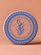 Round ceramic coaster featuring a silhouetted dancing figure reaching toward a crescent moon, surrounded by concentric rings of stars and floral patterns in blue on peach background