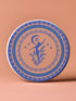 Round ceramic coaster featuring a silhouetted dancing figure reaching toward a crescent moon, surrounded by concentric rings of stars and floral patterns in blue on peach background