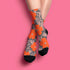 Colorful mid-calf crew socks featuring a bold orange hibiscus floral pattern layered over wavy zebra stripes in taupe and gray, with black heels and toes.