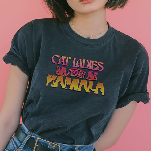 Faded vintage Black t-shirt with "Cat Ladies for Kamala" in retro-style pink and yellow lettering. Cat silhouettes accent the text.