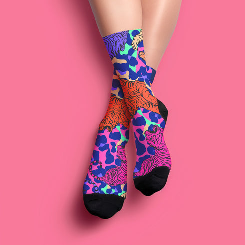 Stylish jungle-themed socks with tigers and abstract camo patterns in a palette of purple, blue, and pink, laid out on a yellow background, ideal for adding a pop of color to your wardrobe
