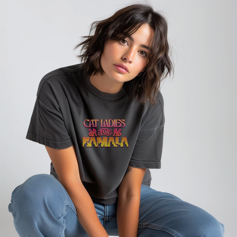 Faded vintage Black t-shirt with "Cat Ladies for Kamala" in retro-style pink and yellow lettering. Cat silhouettes accent the text.