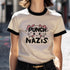 Off-white ringer t-shirt with black contrast trim on the collar and sleeve cuffs. The front features a bold, kawaii-inspired graphic of a cute cat with pink bows, blushing cheeks, and an assertive expression. Above the cat, the phrase "PUNCH" is written in bold, black capital letters, while below, "NAZIS" is displayed in a matching bold font. The cat’s paws are raised, playfully flipping off the viewer, adding a rebellious edge to the design. The t-shirt has a vintage-inspired fit, made from soft cotton fab