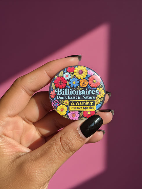 A round pinback button featuring a flat-printed design that mimics the appearance of highly detailed, 3D embroidery (trompe-l'œil). The background is solid black, with a floral border including red, yellow, sky blue, magenta, and orange flowers. In the center, the text "Billionaires Don't Exist in Nature" is written in a blue serif font. Below the text is a yellow rectangle with black borders containing a warning icon and the words "Warning: Invasive Species" in a bold, sans-serif black font.