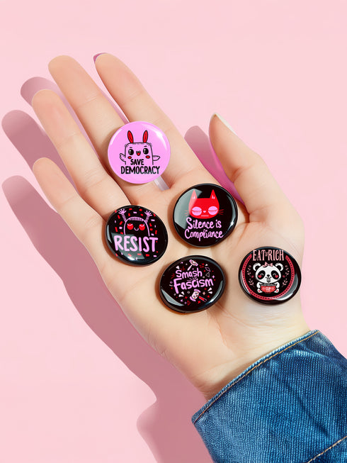 A set of five glossy round pinback buttons with pastel goth and kawaii punk designs, featuring slogans like "Eat The Rich" and "Smash Fascism" in bold pink and black. Each pin has a cute character delivering a powerful message.