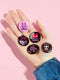 A set of five glossy round pinback buttons with pastel goth and kawaii punk designs, featuring slogans like "Eat The Rich" and "Smash Fascism" in bold pink and black. Each pin has a cute character delivering a powerful message.