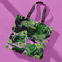 Tote bag with black handles featuring vibrant yellow and blue tigers on a background of pink and black with green foliage
