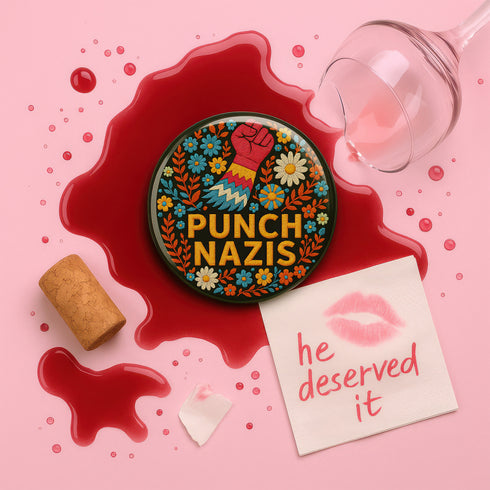 Round black pinback button with bold embroidered-style design featuring a raised red fist, zigzag sleeve, and colorful folk art flowers in orange, teal, yellow, and white. Center text reads “PUNCH NAZIS” in bright golden thread-style lettering. The design is bold, anti-fascist, and maximalist, shown on a glossy pin surface against a pink and purple gradient background. Statement accessory for protest fashion, punk style, and political activism.