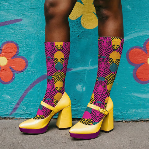 Colorful pink tiger print crew socks with black heel and toe, featuring yellow zebra stripes and teal and coral fan-shaped accents. Made of stretchy knit with a bold maximalist aesthetic. One size fits most, mid-calf length, vibrant all-over print