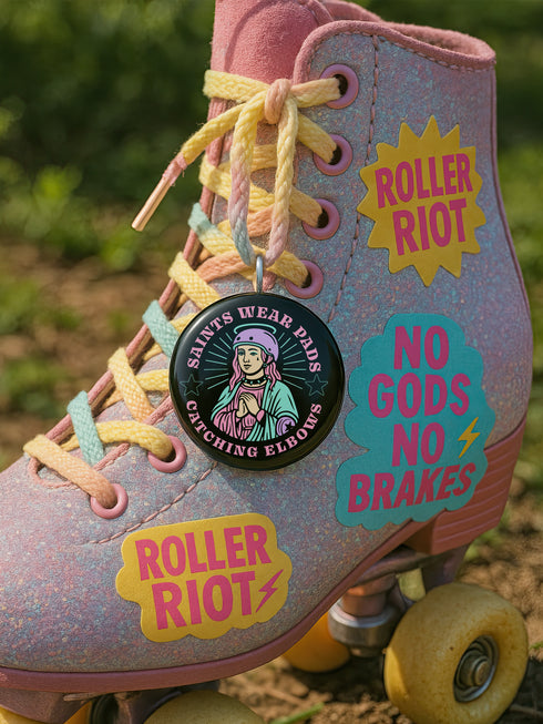 Pinback button badge featuring a saint-inspired roller skater wearing pads and a helmet, with pink hair and teal robes. Surrounded by retro starbursts, the black button reads “Saints Wear Pads Catching Elbows” in pastel pink and teal lettering. Design is bold, colorful, and printed on a glossy metal surface with a classic safety pin back. Available in 2.25" or 3" sizes.